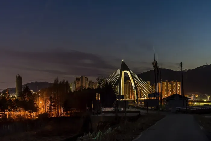 Framed Print : Night view of concrete bridge with triangular arch over a river with community buildings in background