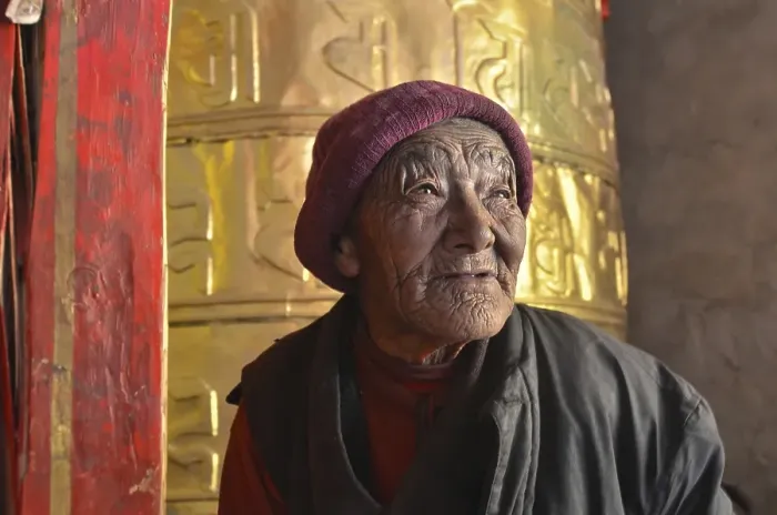 Framed Print : Nun, 76 years, in front of a huge golden prayer wheel Framed Print : Nun, 76 years, in front of a huge golden prayer wheel