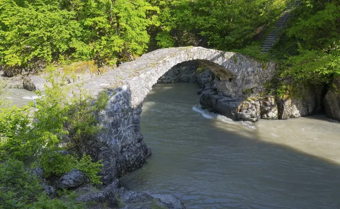 Framed Print : Old stone bridge spanning river in a green forest area in sunshine
