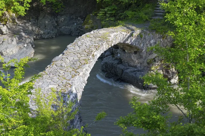 Framed Print : An old stone bridge spans a river amid green trees and rocks