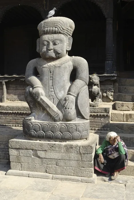 Framed Print : Old woman seated by a large stone statue of a Malla wrestler in front of Dattatreya Temple