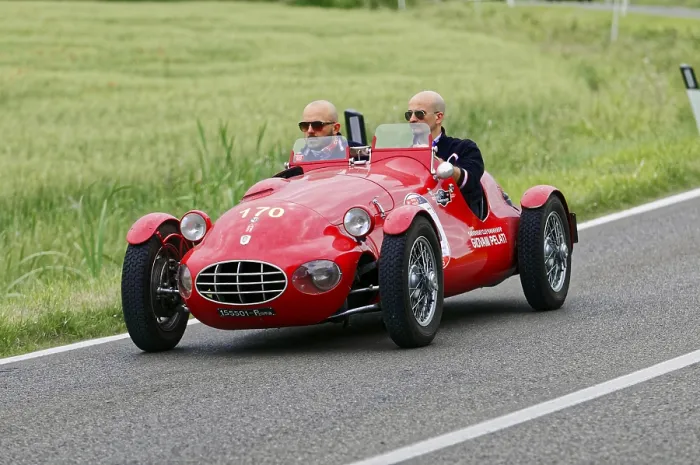 Framed Print : An open red sports car with two drivers drives through a green landscape