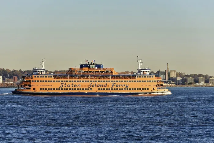 Framed Print : Orange-coloured Staten Island Ferry on water against a city backdrop