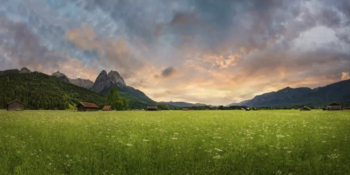 Framed Print : Panoramic view of a green meadow in front of imposing mountains under a cloudy evening sky Framed Print : Panoramic view of a green meadow in front of imposing mountains under a cloudy evening sky