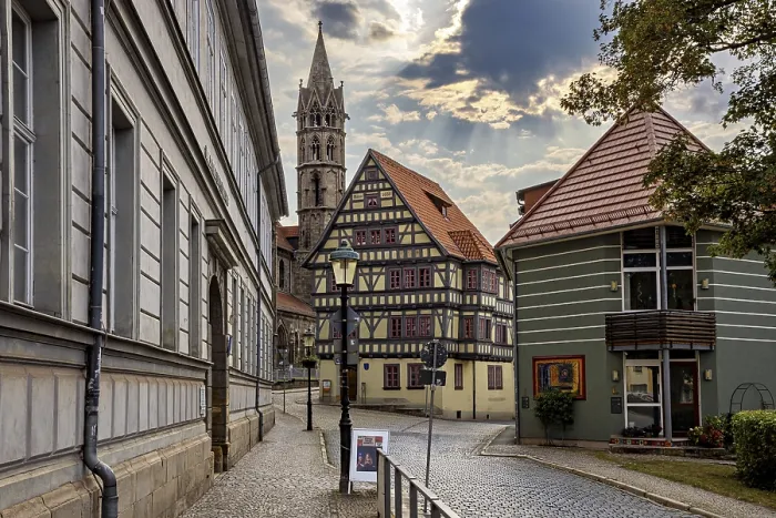 Framed Print : Paved street with half-timbered houses and church tower under a cloudy sky