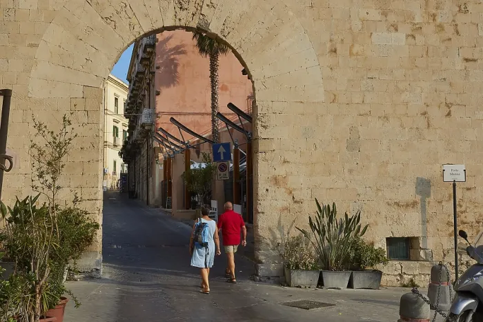 Framed Print : People crossing a historic stone city gate surrounded by plants