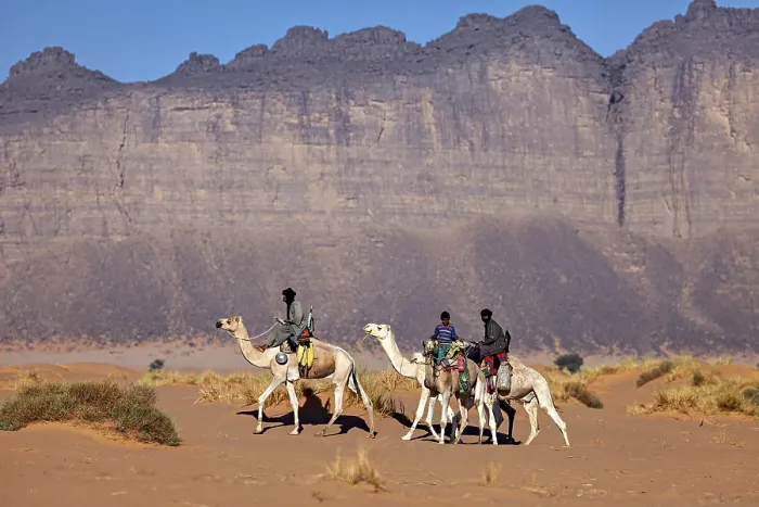 Framed Print : Three people riding camels through an arid desert landscape in front of imposing rock formations Framed Print : Three people riding camels through an arid desert landscape in front of imposing rock formations