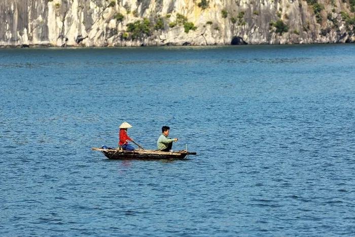 Framed Print : Two people in a small boat in front of a rocky coast with deep blue water Framed Print : Two people in a small boat in front of a rocky coast with deep blue water