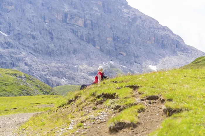 Framed Print : Person sitting on a green meadow with rocky mountains in the background