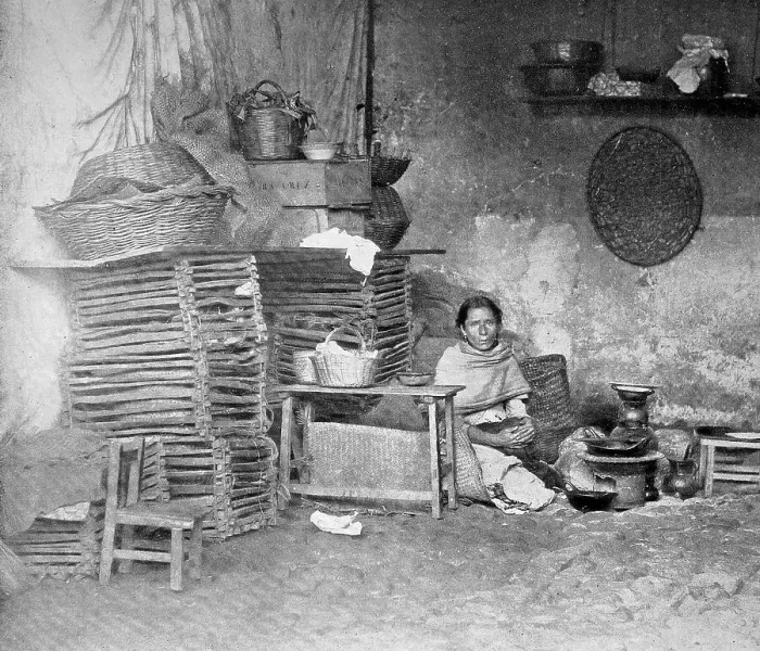 Framed Print : Poor Mexican woman sitting in her kitchen at the charcoal kettle and next to her is a stack of woven baskets