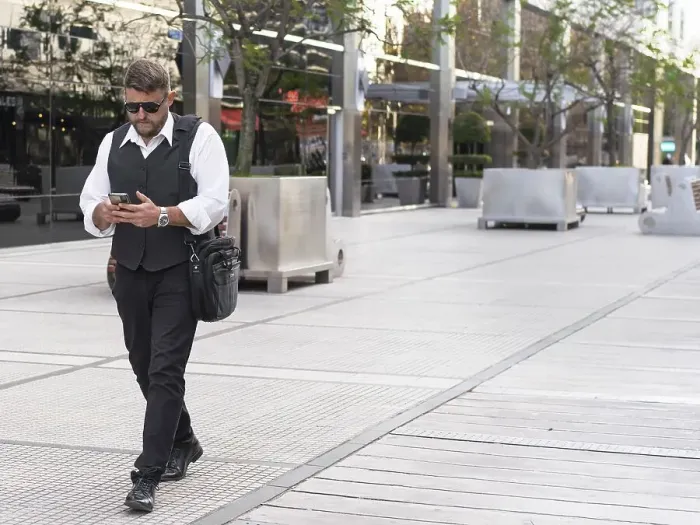 Framed Print : Portrait of a businessman walking on the street while he sends messages on his mobile phone