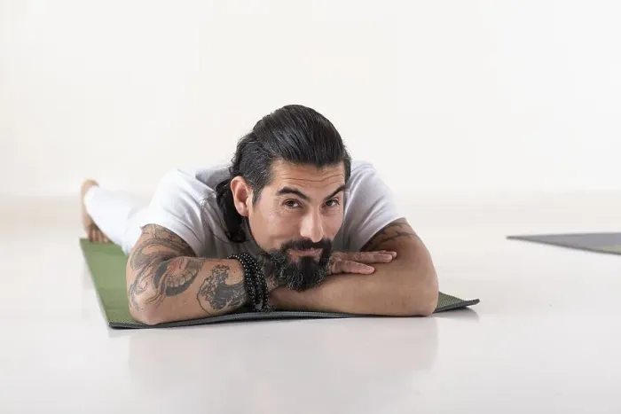Framed Print : Portrait of a young man dressed in white yoga clothes lying on a mat while looking at camera over white background