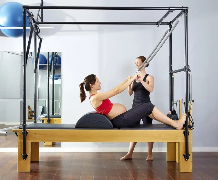 Framed Print : Pregnant woman pilates reformer roll up cadillac exercise with personal trainer