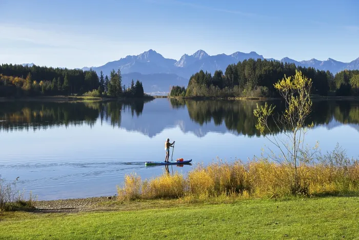 Framed Print : A quiet lake surrounded by mountains and forests with a person on a paddleboard in autumn