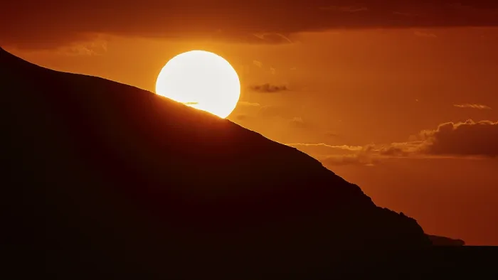 Framed Print : Radiant sun over a mountain in an intense orange sky at sunset