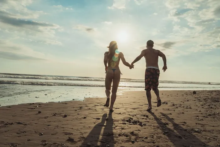 Framed Print : Rear view of couple running hand in hand along a sandy beach at sunset