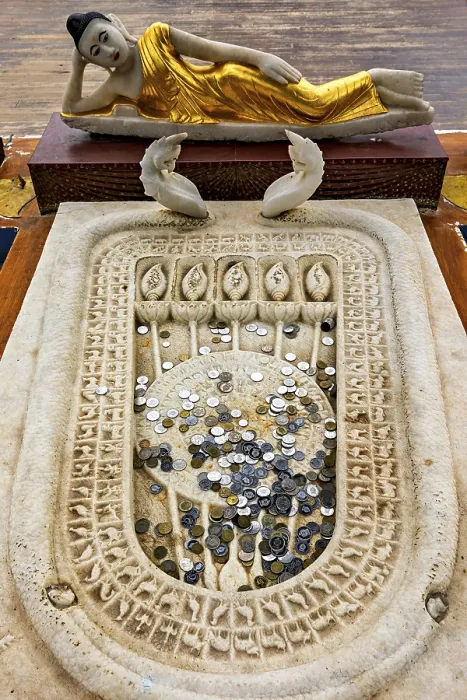 Framed Print : A reclining Buddha statue with gold robes above a carved stone surface filled with coins Framed Print : A reclining Buddha statue with gold robes above a carved stone surface filled with coins