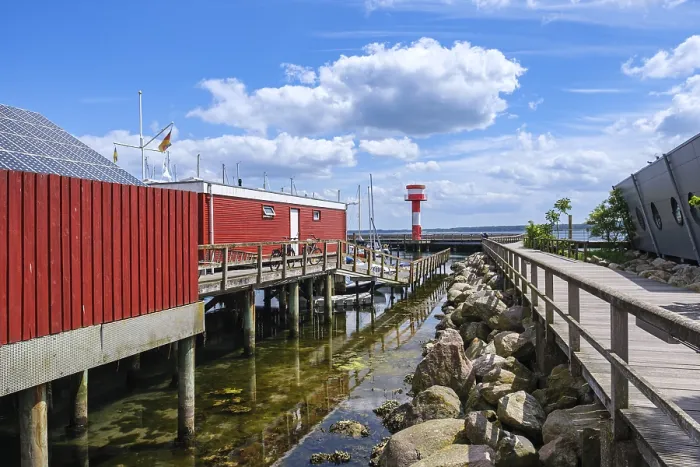Framed Print : A red building on the waterfront with a jetty and rocks on the shore under a blue sky Framed Print : A red building on the waterfront with a jetty and rocks on the shore under a blue sky