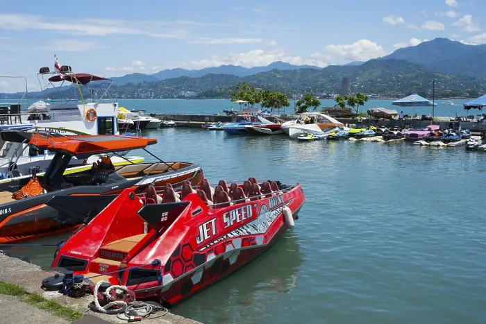 Framed Print : A red jet boat in the foreground of a harbor surrounded by other boats and mountains in the background