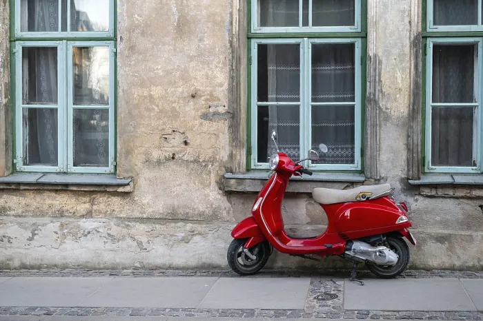 Framed Print : A red vintage scooter on a pedestrian sidewalk in front of an old stone house