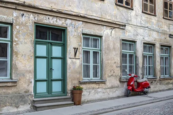 Framed Print : A red vintage scooter on a pedestrian sidewalk in front of an old stone house Framed Print : A red vintage scooter on a pedestrian sidewalk in front of an old stone house