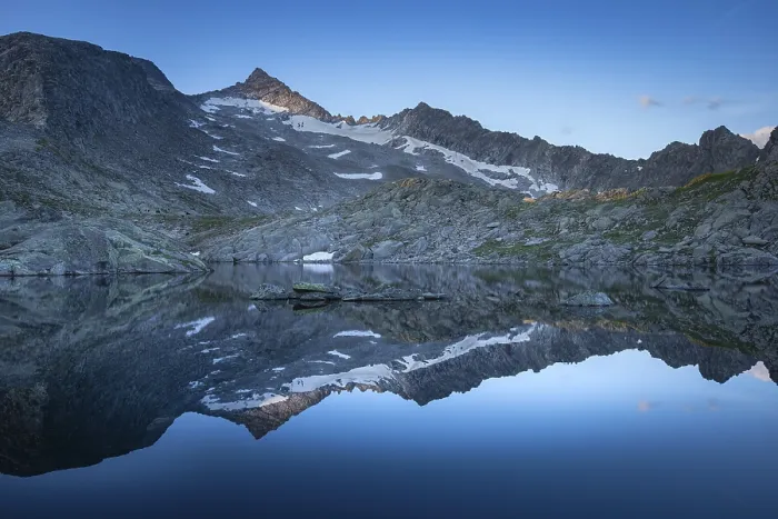 Framed Print : Reflection of snow-covered mountains on a calm water surface under a blue sky at sunrise