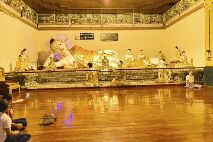 Framed Print : Resting Buddha statue in a gold-decorated interior with meditation participants