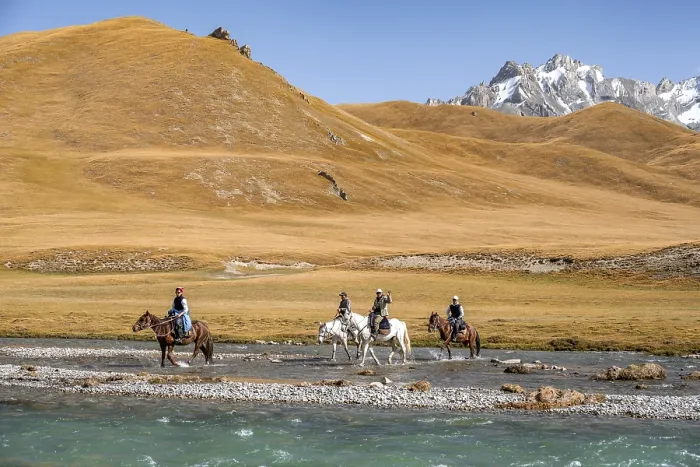 Framed Print : Riders riding through river in front of mountain landscape with yellow meadows Framed Print : Riders riding through river in front of mountain landscape with yellow meadows