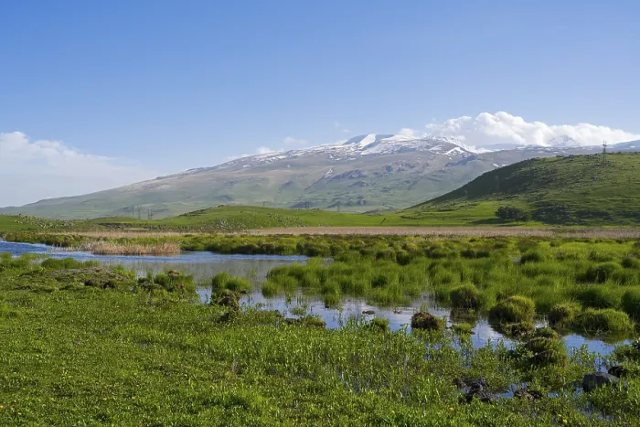 Framed Print : A river meanders through green hills in front of a mountain range with a slightly cloudy sky Framed Print : A river meanders through green hills in front of a mountain range with a slightly cloudy sky
