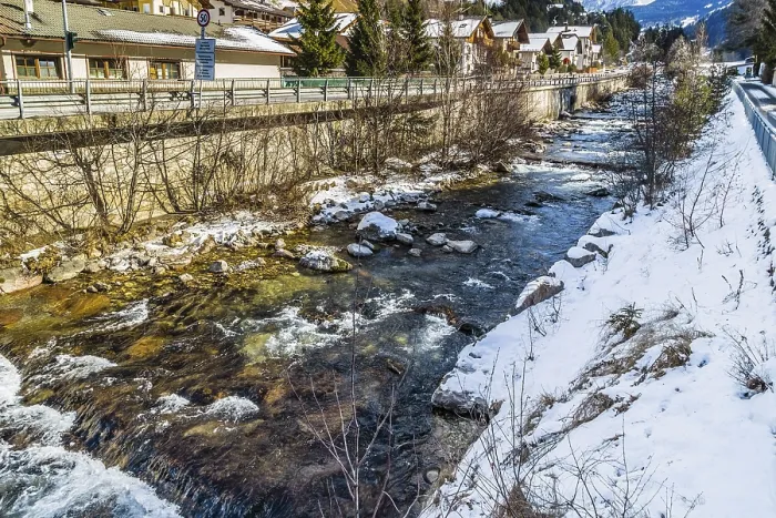 Framed Print : River passing through snowy alpine village in Italy illuminated by sun with mountains in the background Framed Print : River passing through snowy alpine village in Italy illuminated by sun with mountains in the background