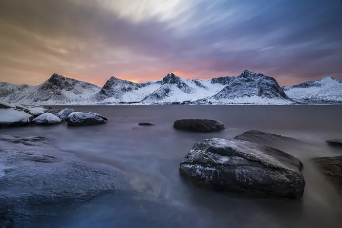 Framed Print : Rocky coast at the fjord with snow-covered mountains at sunset
