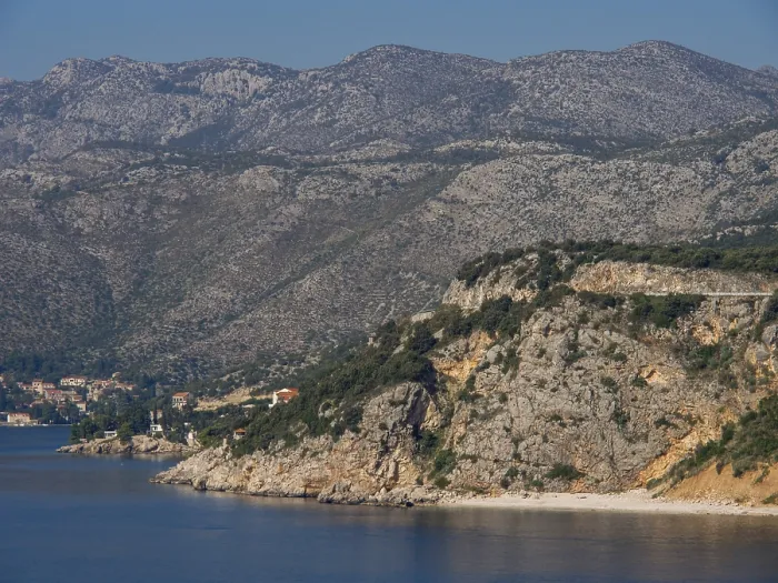 Framed Print : Rough coastline with large rocks and massive mountains behind them on the clear sea