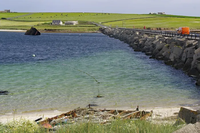 Framed Print : Ruin of a boat on the beach with a breakwater and green coastal background