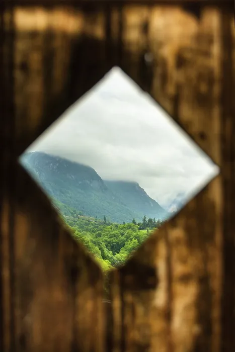 Framed Print : Rustic wooden frame reveals a lush green landscape with mountains in the background under a cloudy sky Framed Print : Rustic wooden frame reveals a lush green landscape with mountains in the background under a cloudy sky