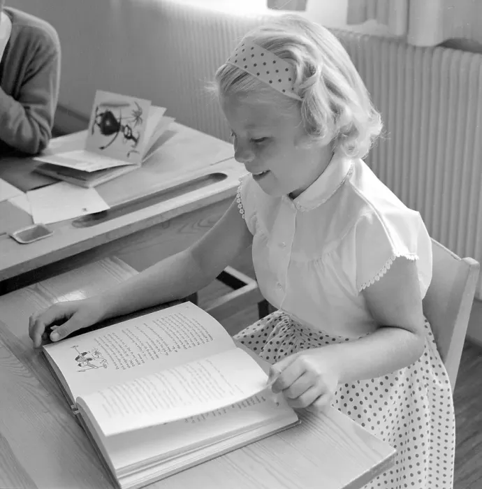 Framed Print : School in the 1950s. A girl is seen sitting at her desk in the classroom reading from the schoolbook in front of her