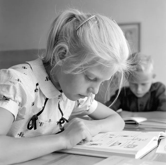 Framed Print : School in the 1950s. A girl is seen sitting at her desk in the classroom reading from the schoolbook in front of her