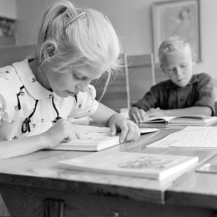 Framed Print : School in the 1950s. A girl is seen sitting at her desk in the classroom reading from the schoolbook in front of her