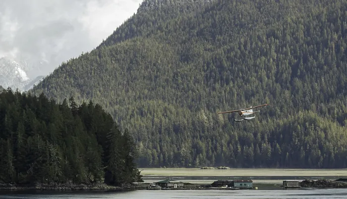 Framed Print : A seaplane flies over a tranquil lake surrounded by dense forest and mountains under an overcast sky in Tofino
