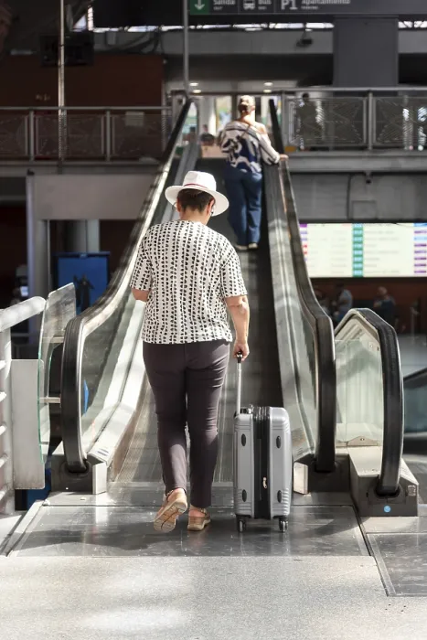 Framed Print : Senior woman in white hat pulling suitcase up an escalator inside modern transport terminal