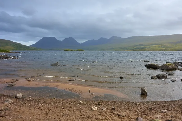 Framed Print : Shores of a lake with waves and mountains in the background under cloudy sky