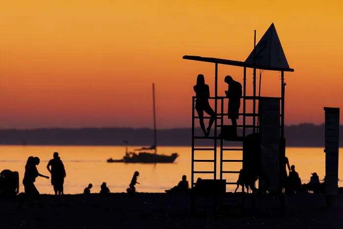 Framed Print : Silhouetted figures against an orange sunset on the beach with a lifeguard tower