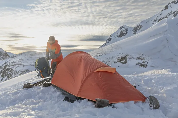 Framed Print : A ski tourer sets up near a bright orange tent amidst snowy mountains at sunrise