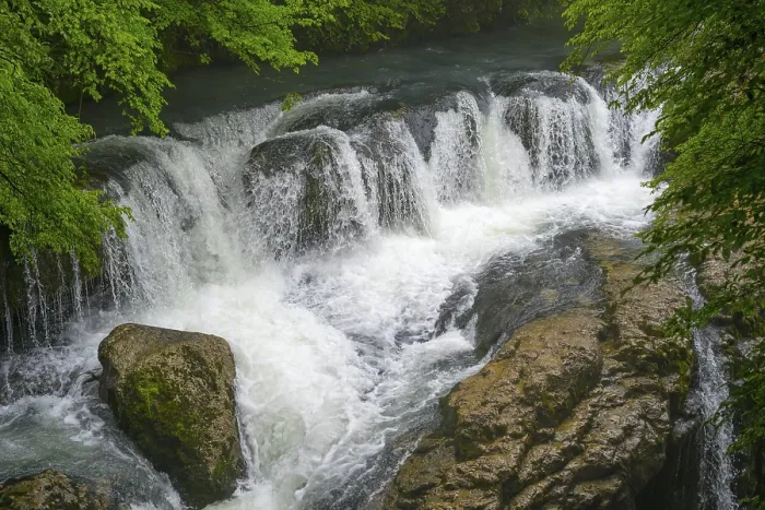 Framed Print : Small waterfall over rocks in a river surrounded by green trees