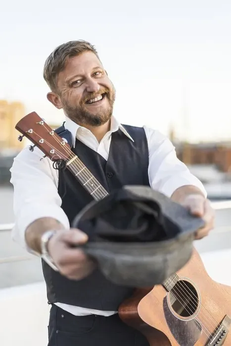 Framed Print : A smiling street musician looking at camera and carrying his guitar while asking for tips