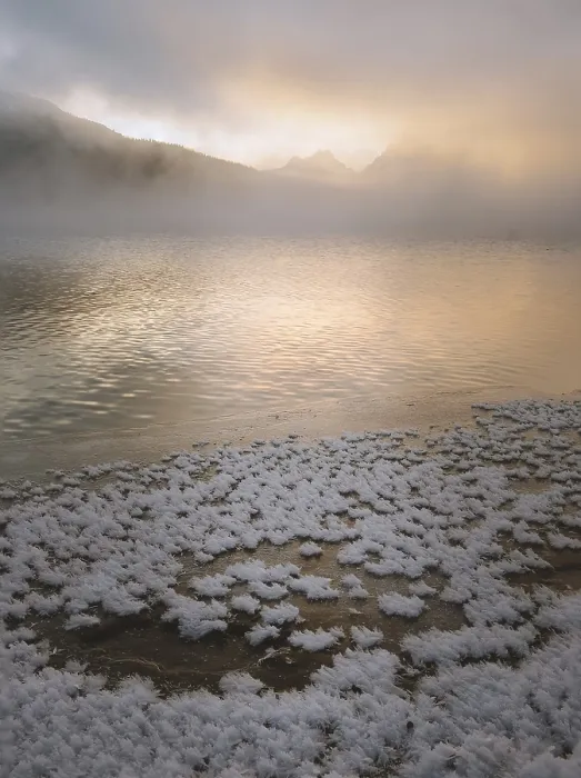 Framed Print : Snow-covered lake shore with distant misty mountains under a golden sunrise