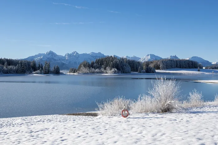 Framed Print : Snowy lakeside landscape with mountains in the background and clear sky