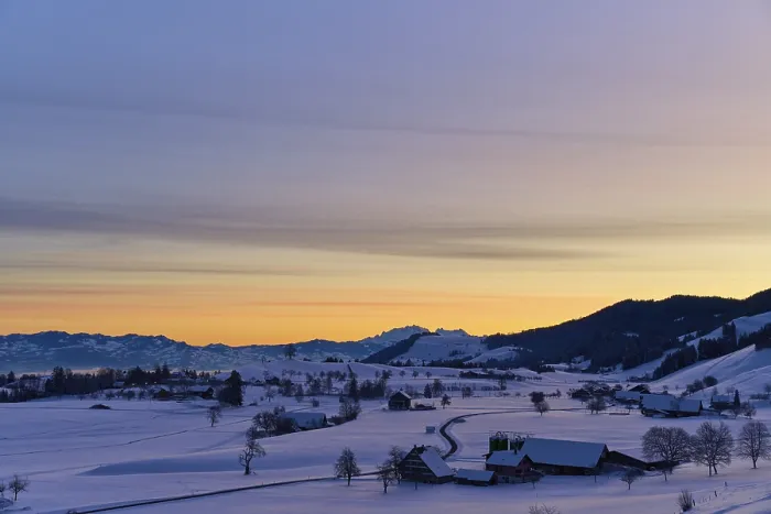 Framed Print : Snowy landscape at sunrise with mountains and farms