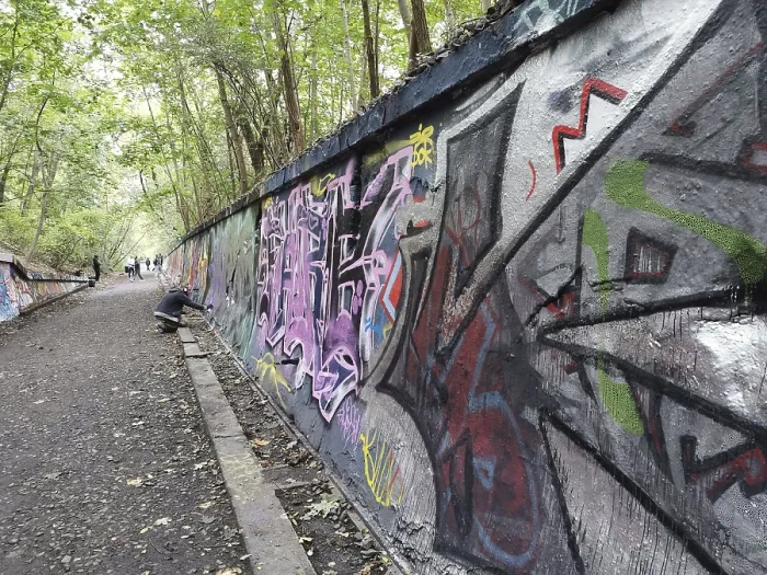 Framed Print : Sprayers spray colorful graffiti art on a long wall along a forest