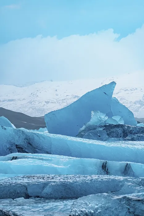 Framed Print : A stark blue iceberg rises against a cold wintry sky with snowy peaks in the distance