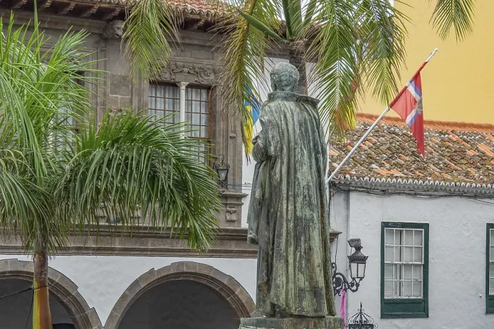 Framed Print : Statues and palm trees in front of colonial building with flags in a square